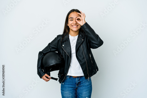 Young asian woman holding a motorbike helmet over isolated background excited keeping ok gesture on eye.