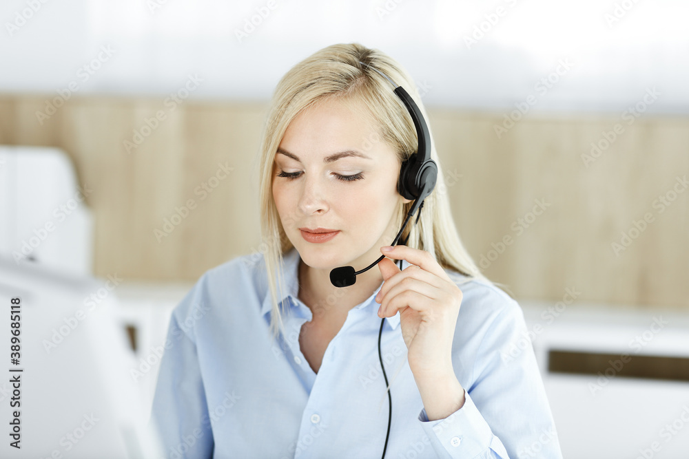Blonde business woman sitting and communicated by headset in call center office. Concept of telesales business or home office occupation Blonde business woman sitting and communicated by headset in call center office. Concept of telesales business or home office occupation