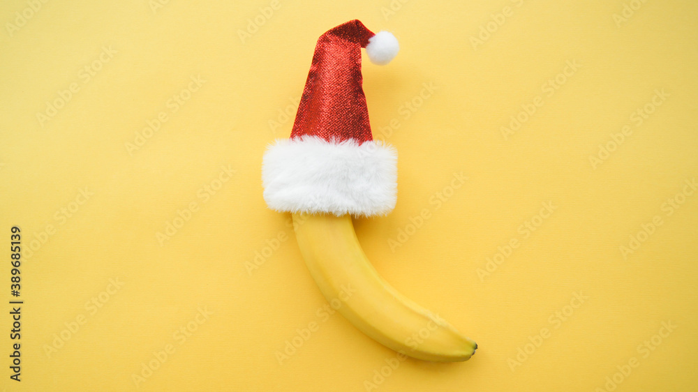 Fresh natural banana fruit in a red Santa Claus hat on the yellow background. Merry Christmas