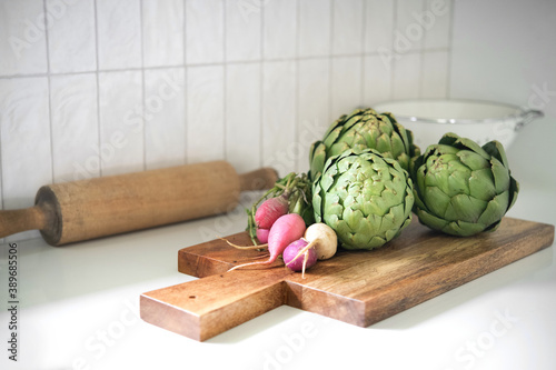 Artichoke and radishes on a cutting board in a beautiful kitchen photo