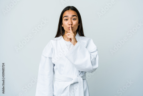 Young asian woman doing karate isolated on white background keeping a secret or asking for silence.