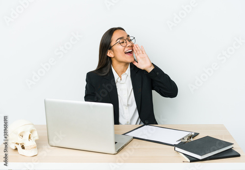 Young traumatologist asian woman isolated on white background shouting and holding palm near opened mouth.