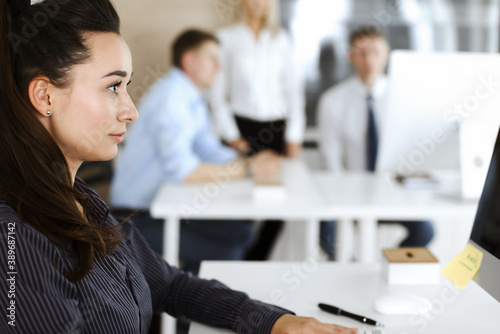 Business woman using computer at workplace in modern office. Brunette secretary or female lawyer looking at the camera and happy smiling. Working for pleasure and success © Iryna