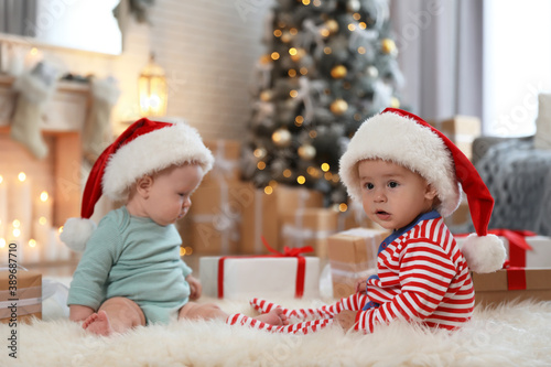 Cute children in Santa hats on floor in room with Christmas tree