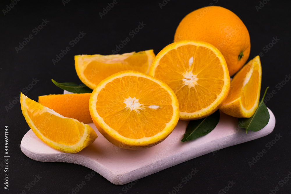 Sliced oranges on a white wooden board on a black background.
Close-up.
Sliced oranges on a white wooden board on a black background.
Close-up.