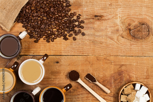 Café solo y café con leche junto a granos de café, un cuenco con azúcar y cucharas sobre una mesa de madera rústica. Vista superior. Copy space photo