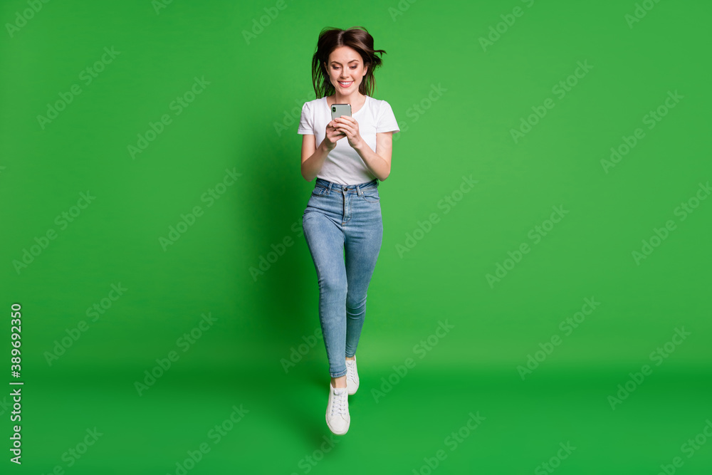 Full size photo of girl jump search social network discount smartphone wear t-shirt jeans isolated green color background Full size photo of girl jump search social network discount smartphone wear t-shirt jeans isolated green color background