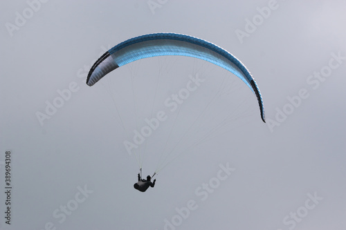 Paraglider flying blue wing in a cloudy sky