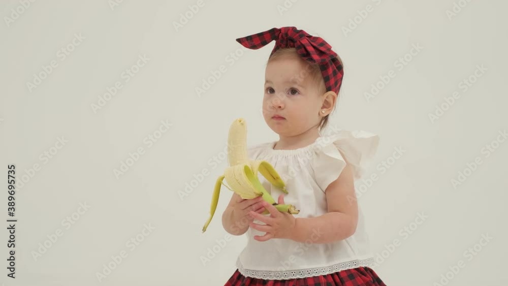 Little girl in plaid headband got a peeled banana. Close up slow motion.