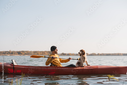 Tableau sur toile Kayaking with dogs: man rowing a boat on the lake with his spaniel