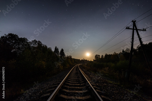 the railroad leads towards the rising full moon on a clear starry night