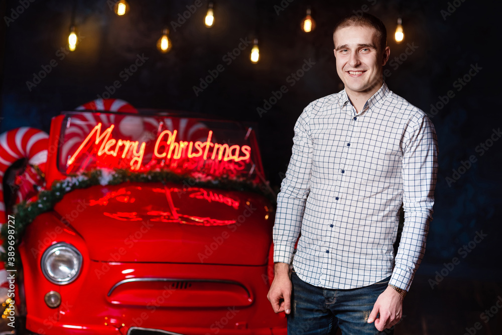 handsome man in the christmas studio against the background of glowing lights and retro car.