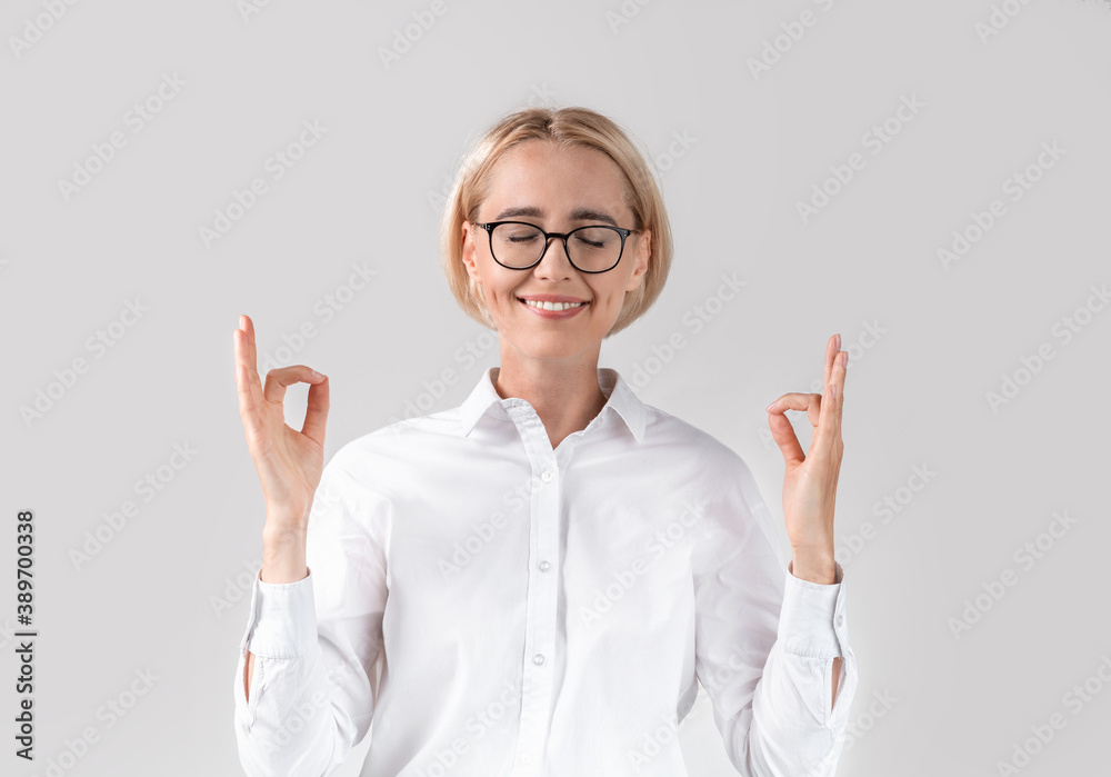 Stress management concept. Calm mature business lady in office wear meditating on light grey studio background Stress management concept. Calm mature business lady in office wear meditating on light grey studio background