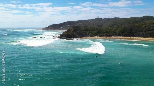 Wide cinematic drone shot of surfers in the water and island in background at Wategos Beach Australia photo