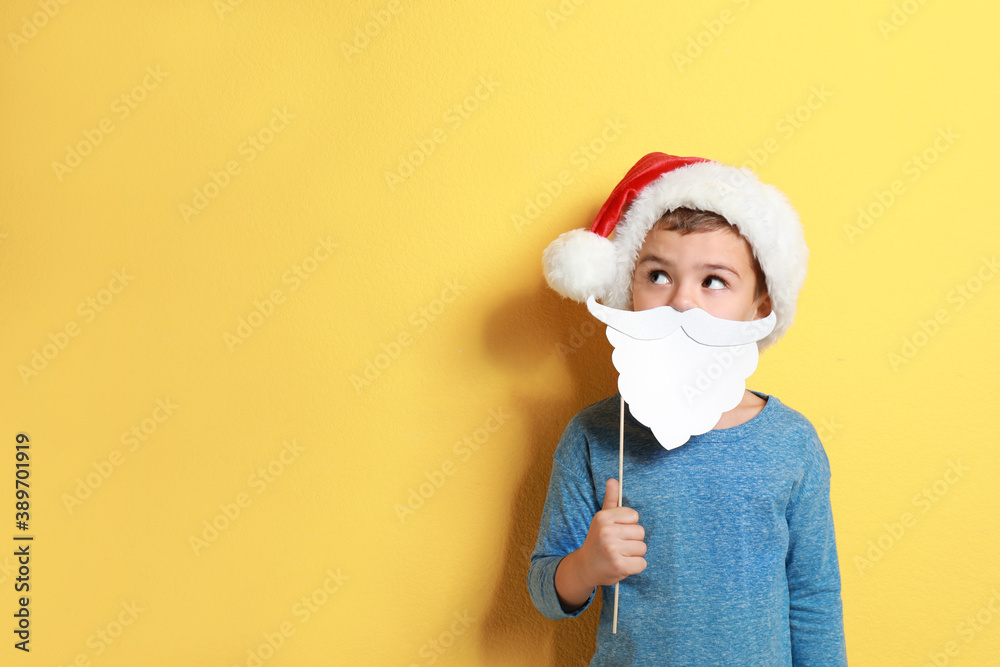 Cute little boy with Santa hat and white beard prop on yellow background, space for text. Christmas celebration Cute little boy with Santa hat and white beard prop on yellow background, space for text. Christmas celebration