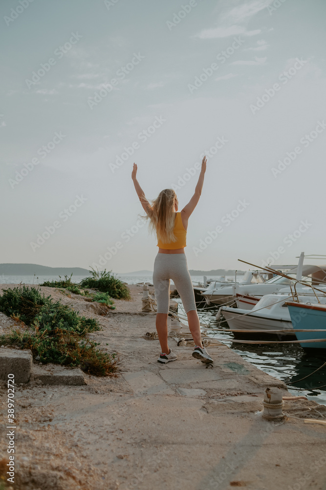 A joyful girl against the background of the sea raised her hands up. Vacation, freedom. Woman on the background of yachts and ships