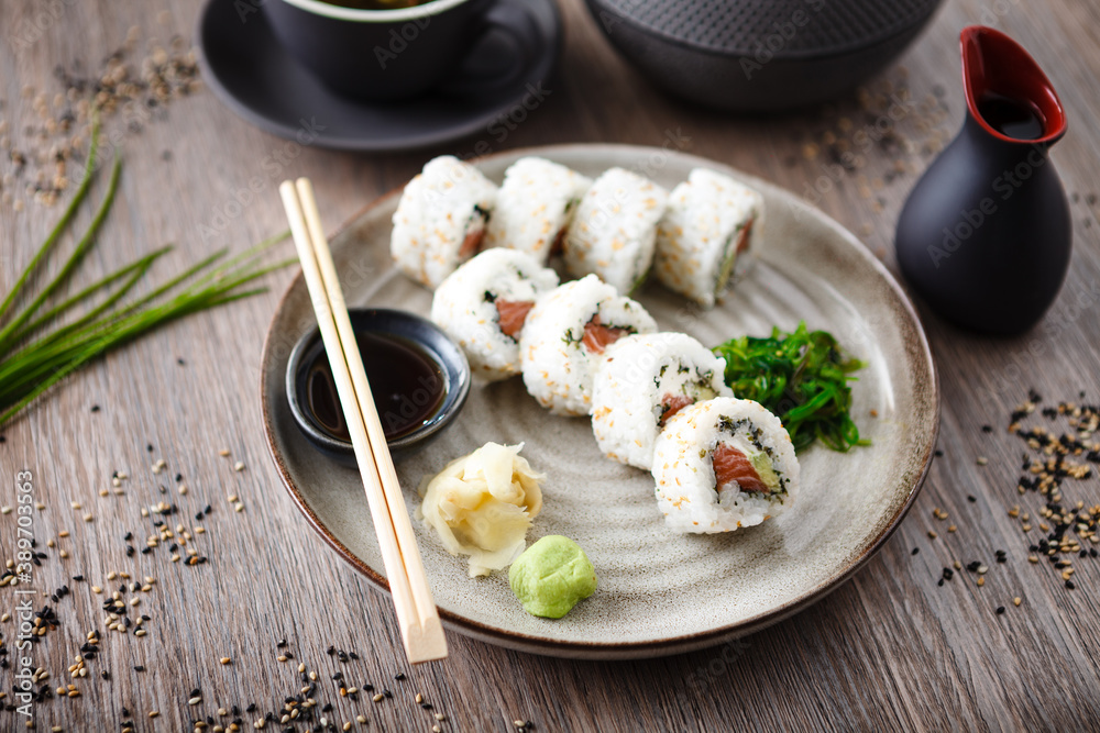 Sushi maki rolls Philadelphia with salmon, creamy cheese and avocado on a plate with chopsticks, soy sauce, wasabi and ginger. Japanese traditional seafood served for lunch in modern restaurant