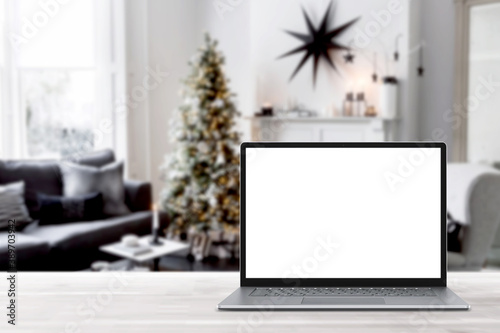 Blank display screen laptop computer on white wood table. Modern cozy comfortable home living room with Christmas decor. Home office desk workspace. Mock up copy space. Winter sales, online shopping