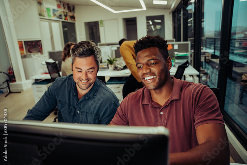 Mixed race business men working on assignment report working late hours in office typing on desktop computer 