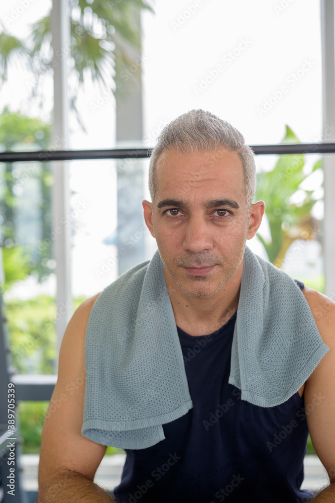 Portrait of mature handsome Persian man sitting at the gym Portrait of mature handsome Persian man sitting at the gym
