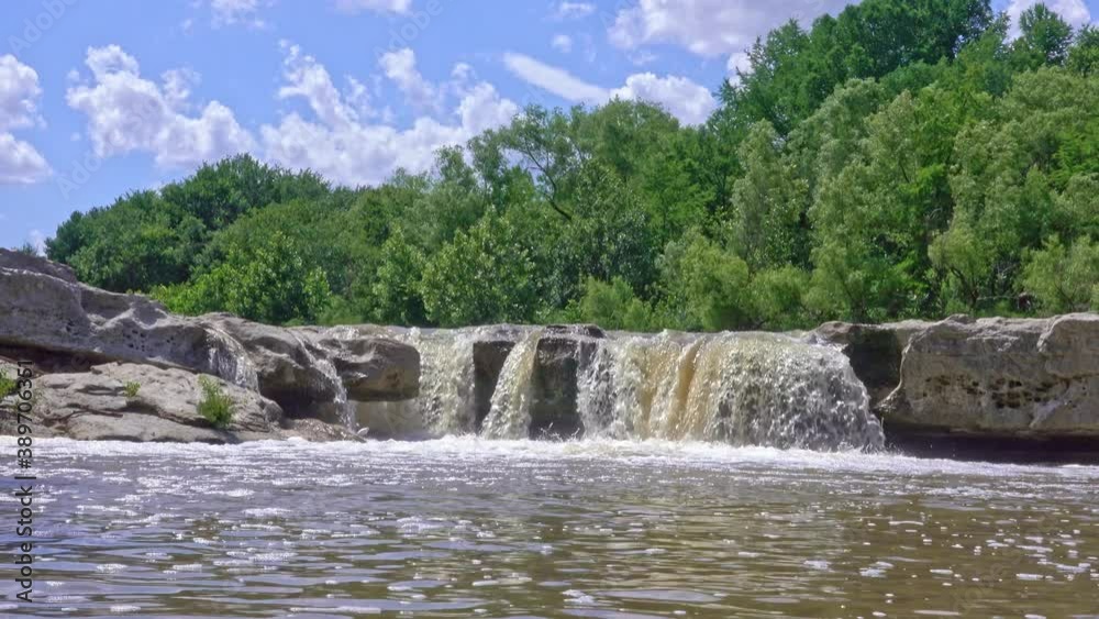 Small waterfall shot at low angle with green trees and blue sky Small waterfall shot at low angle with green trees and blue sky