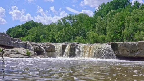 Small waterfall shot at low angle with green trees and blue sky
