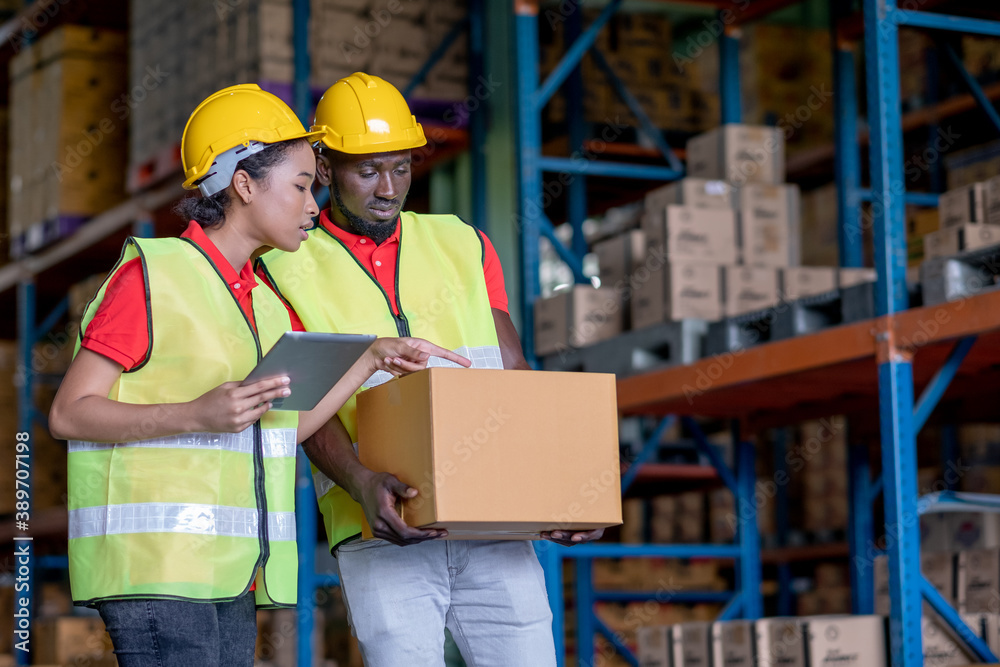 African American warehouse man and woman or factory worker work and discuss together about product box that man holding in workplace area. Concept of good management of staff working. African American warehouse man and woman or factory worker work and discuss together about product box that man holding in workplace area. Concept of good management of staff working.