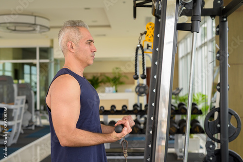 Profile view of mature handsome Persian man exercising at the gym