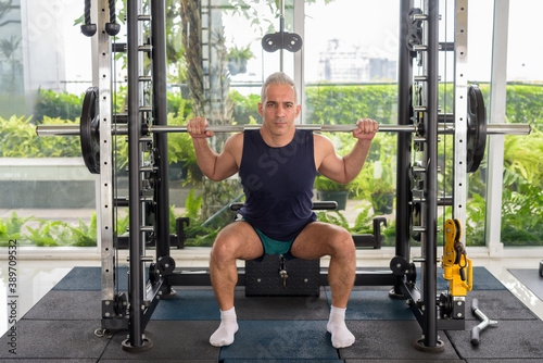 Mature handsome Persian man lifting weight at the gym