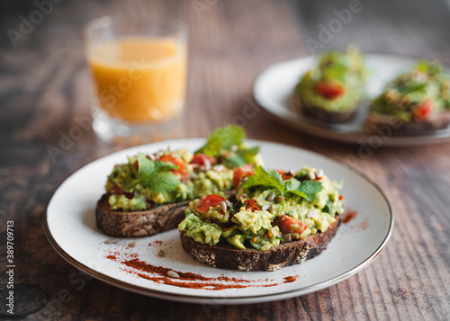 Two avocado toasts on white plate and glass of orange juice