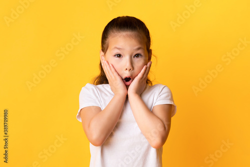 Asian kid with open mouth touching cheeks in excitement
