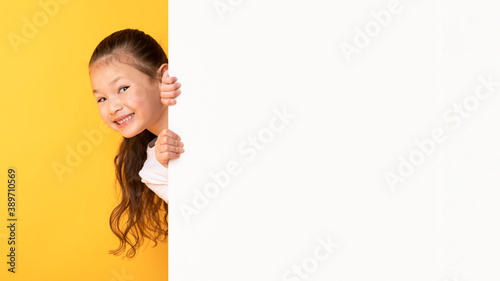 Fényképezés Asian kid hiding behind blank white advertising billboard