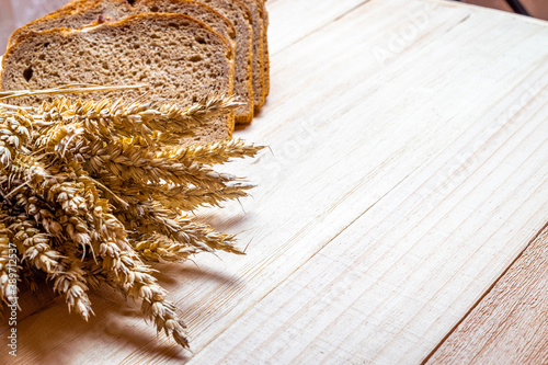 Freshly baked bread. Fresh loaf of rustic traditional bread with wheat grain ear or spike plant on wooden texture background. Rye bakery with crusty loaves and crumbs. Healthy Food concept.