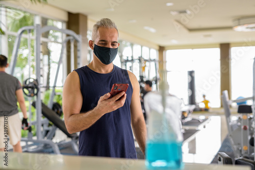 Mature Persian man with mask registering with phone for entrance at the gym