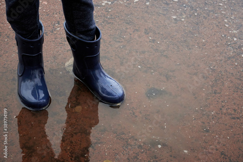 Childs legs in boots stand in puddle after rain.