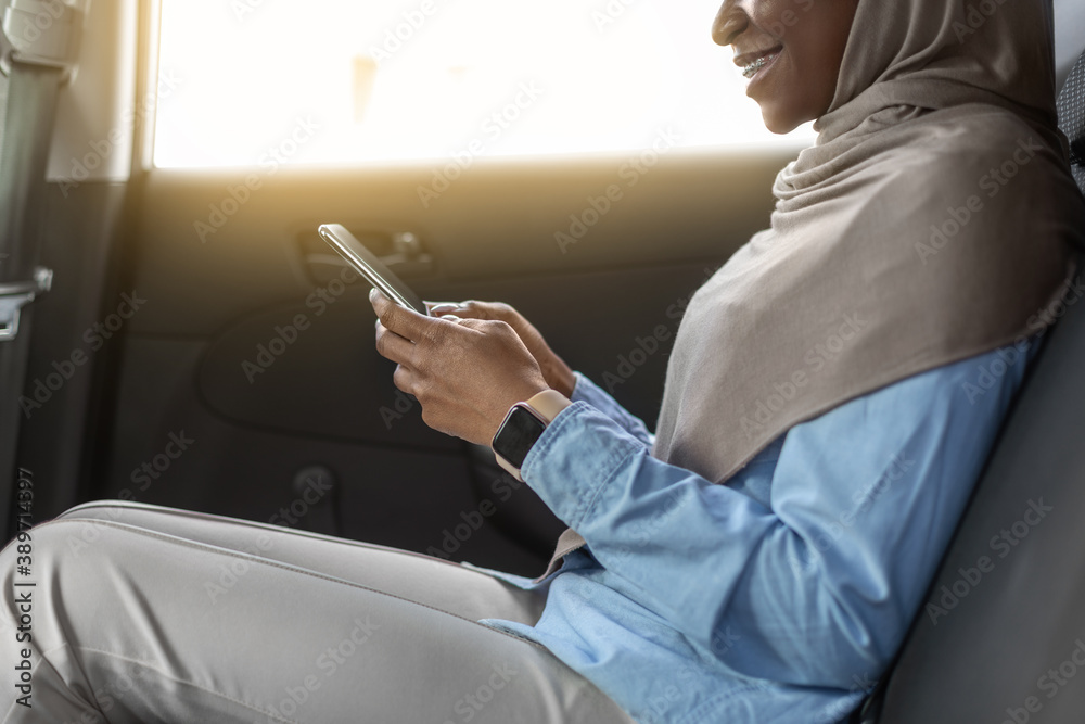 Mobile Communication. Black Businesswoman In Hijab Using Smartphone On Backseat Of Car