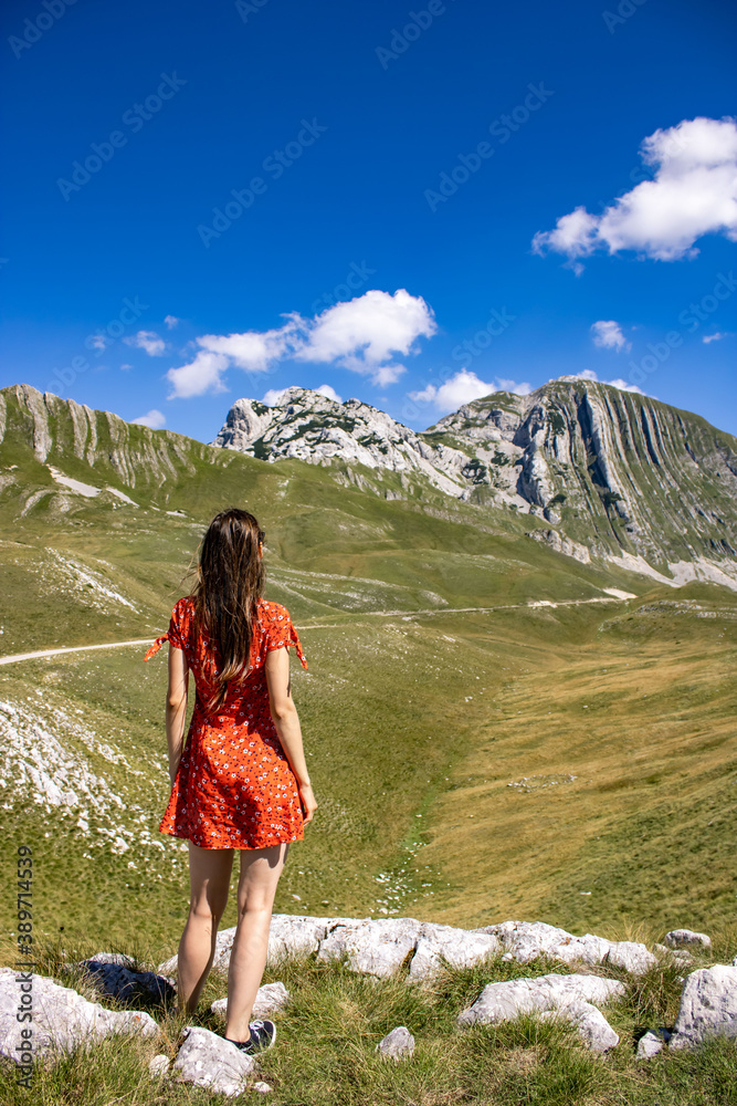 The girl in a red dress against the background of the mountains of Montenegro. Picturesque mountain landscape of Durmitor National Park, Montenegro, Balkans, Dinaric Alps, UNESCO World Heritage Site.
