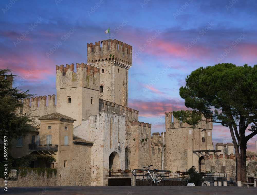 Rocca Scaligera Castle in Sirmione Lake Garda, Italy.  Italian historic castle with the flag of Italy in the background pink clouds at sunset.