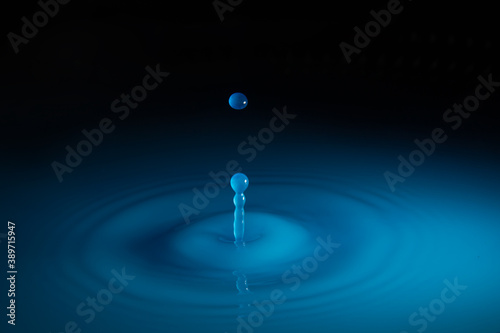 Blue water droplet splashing into blue puddle, making ripples