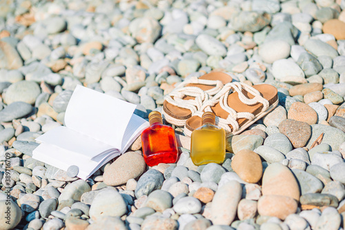 Beach hat on opened book with sunscreen and shoes on pebble beach photo