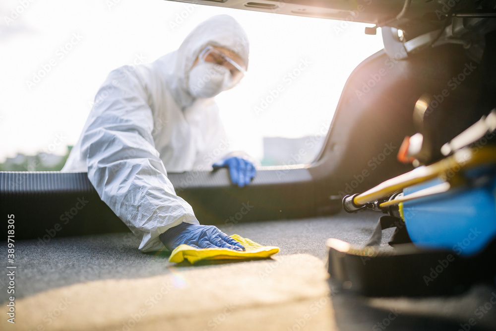 Sanitiry worker disinfects the car's trunk with a yellow rug. A man wearing protective suit, mask and gloves cleans up the trunk's interior of a vehicle. Covid 19 spread prevention concept. Sanitiry worker disinfects the car's trunk with a yellow rug. A man wearing protective suit, mask and gloves cleans up the trunk's interior of a vehicle. Covid 19 spread prevention concept.
