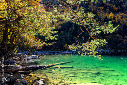 Beautiful autumn landscape with clear green water of a mountain lake and reflected trees with autumn foliage and mountain peaks