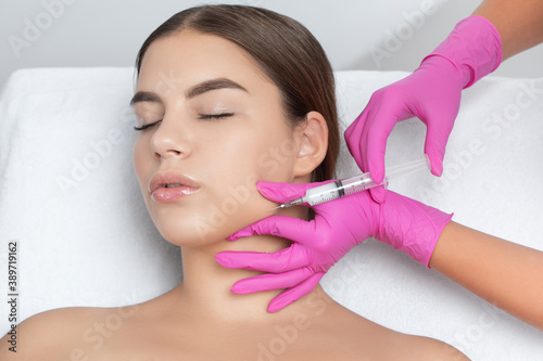 Cosmetologist makes lipolytic injections to burn fat on the chin, cheeks and neck of a woman against double chin. Female aesthetic cosmetology in a beauty salon.Cosmetology concept. photo