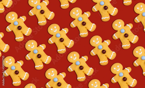 Pattern of delicious gingerbread Christmas cookies in the shape of dolls decorated with icing sugar and candies on red background