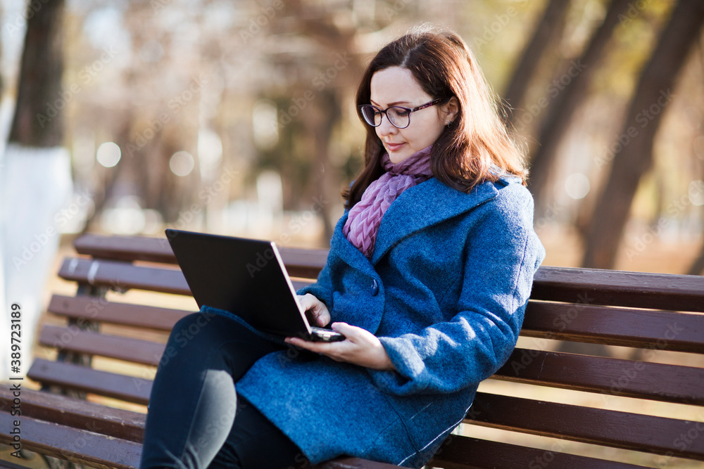Happy young woman working on laptop in autumn at city park.
Happy young woman working on laptop in autumn at city park.