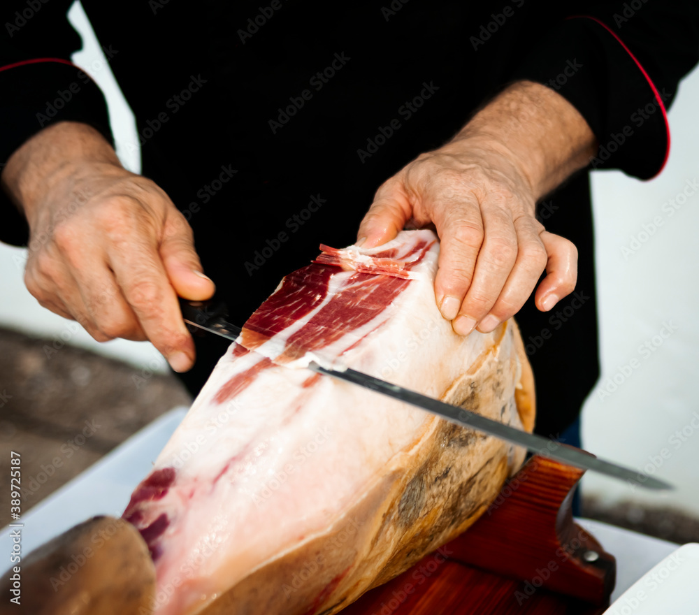 Professional Iberico or Serrano ham cutter is cutting a sliced pork leg with a ham knife