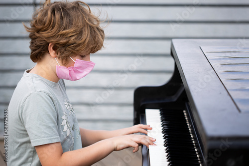 A boy with a mask plays the piano in the park