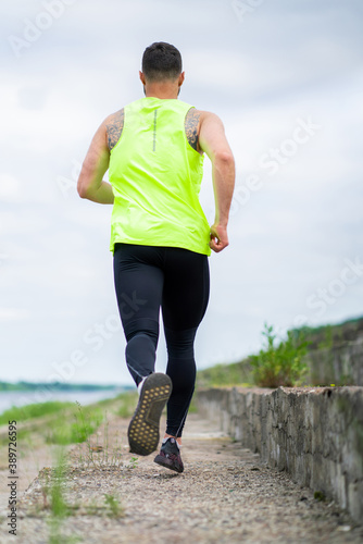 Running athletic guy on workout in stylish sportswear outdoors in cloudy weather, back view