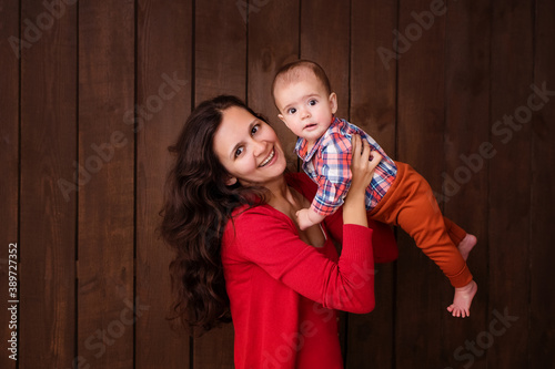 Young woman holding a newborn baby in her arms on the brown background. Newborn photosession. Family portrait. Mother is kissing her baby. Baby goods packing template. Nursery. Medical and healthy.