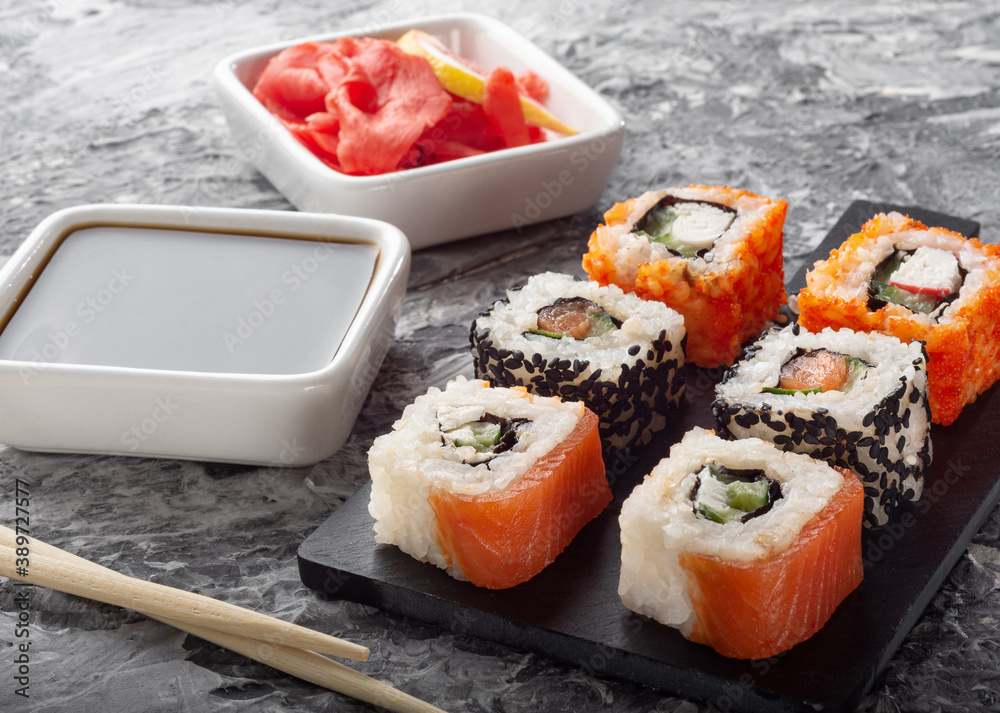 Different rolls on a black Board with soy sauce. Salmon rolls on a dark background. Different rolls on a black Board with soy sauce. Salmon rolls on a dark background.